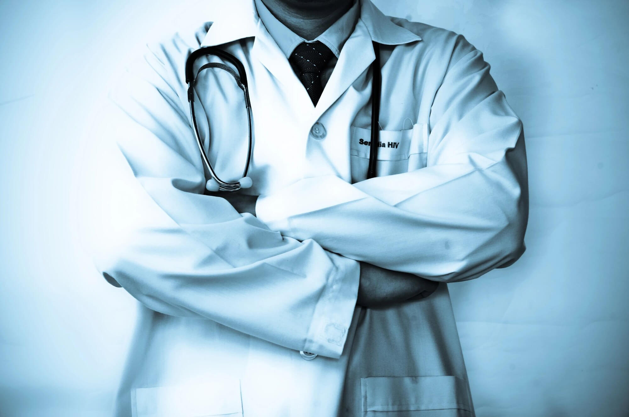 A doctor with his arms crossed wearing a white coat.